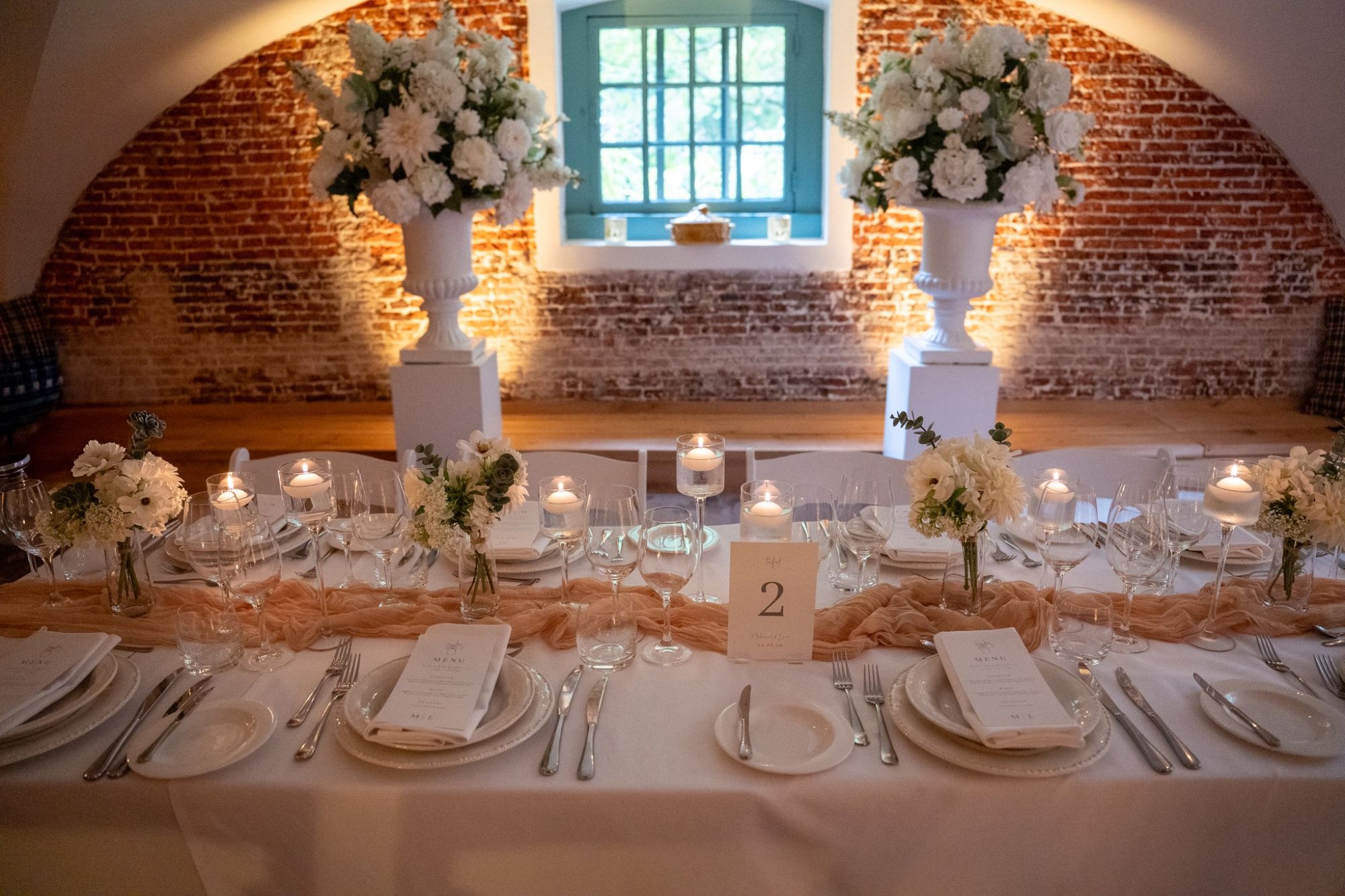 Feesttafel met kaarsen, bloemen en twee witte vazen voor een bakstenen muur